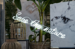 Scritta luminosa Save the Nature tra le piante nell’allestimento Ariostea 2019